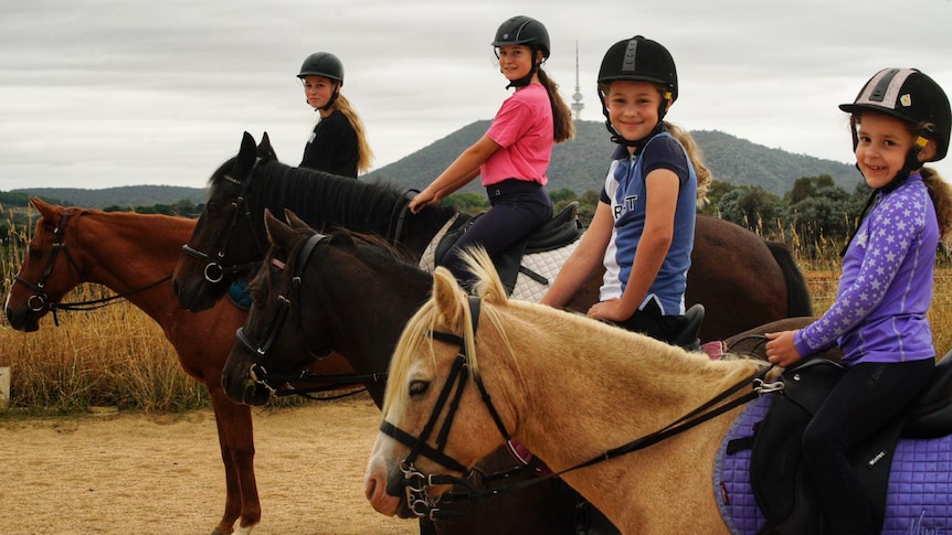 Four young girls ride horses with Telstra Tower in the background.