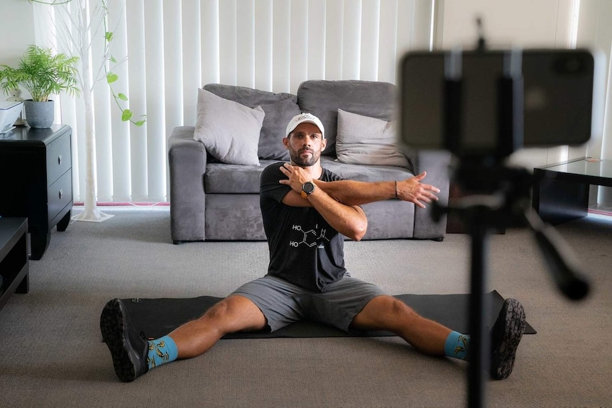 A man sitting on the ground stretching in front of an iPhone mounted on a stand