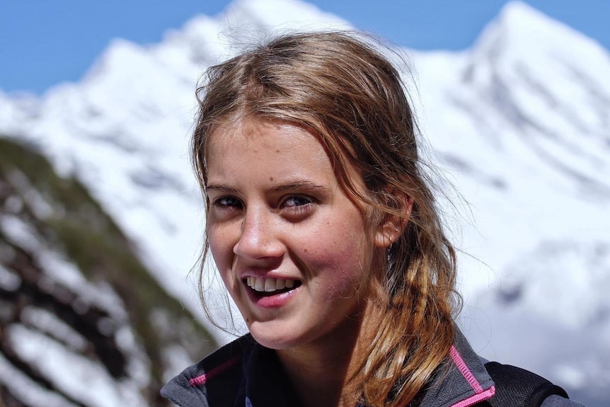 Gabby smiles at the camera. Tall white mountains loom in the background.