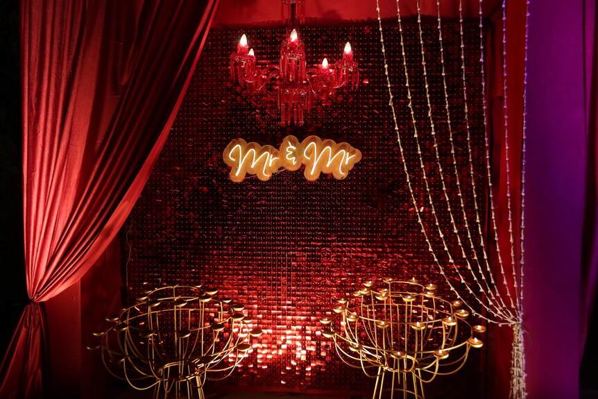 A small stage with red curtains, candles and lit up signs saying "Mr & Mr" for a gay wedding. 
