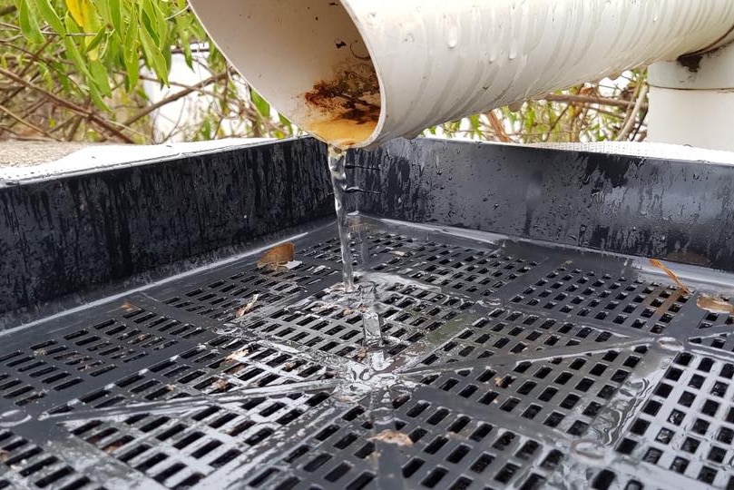 Rain water from a pipe pouring into a water tank