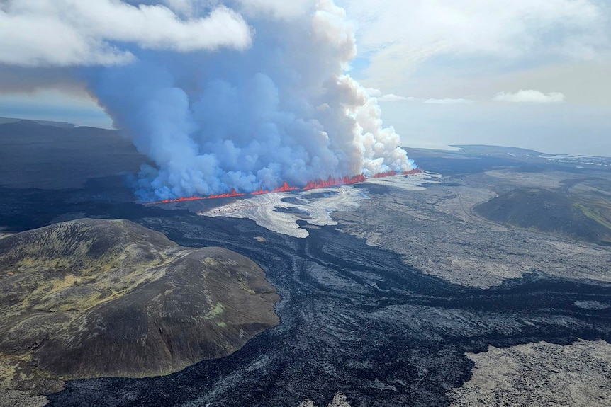 An aerial view of a large fissure with bright orange lava and smoke pouring from it 