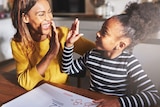 A mother and daughter high five as they do maths equations.