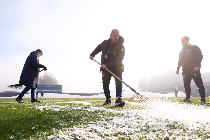 Groundskeepers with rakes try to remove ice from the field before a Chelsea-Liverpool Women's Super League match.