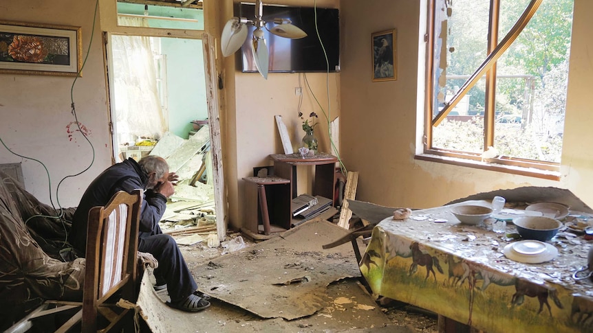 A man cries as he sits in his house damaged by shelling. Kitchenware, ceiling fixtures, furniture are seen damaged.