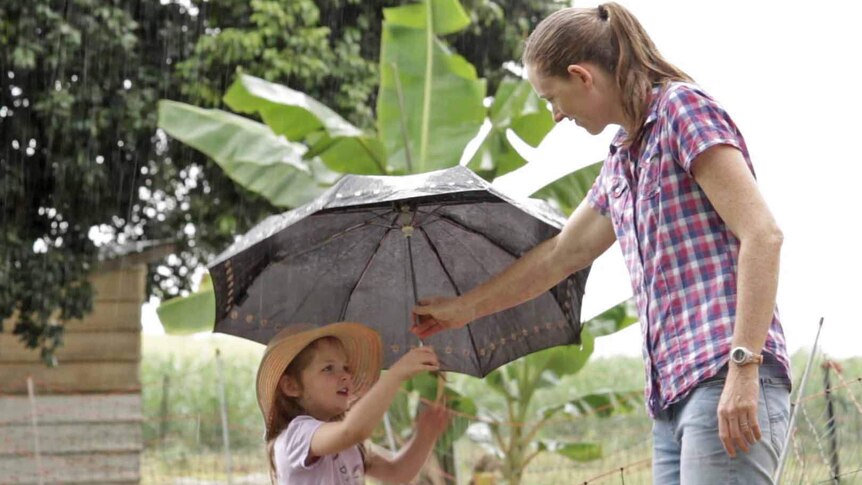 A young girl is handed an umbrella by her mum on a farm