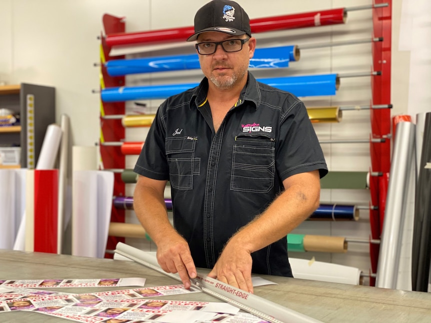 Posters and stickers spread out on a table in front of a man wearing a cap