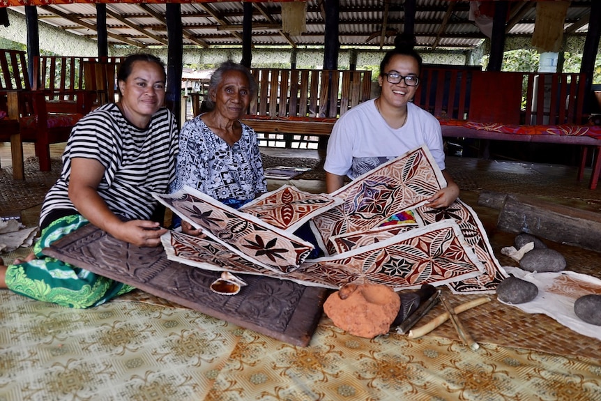 Three women sitting on the floor holding brown flower designed prints in their laps.