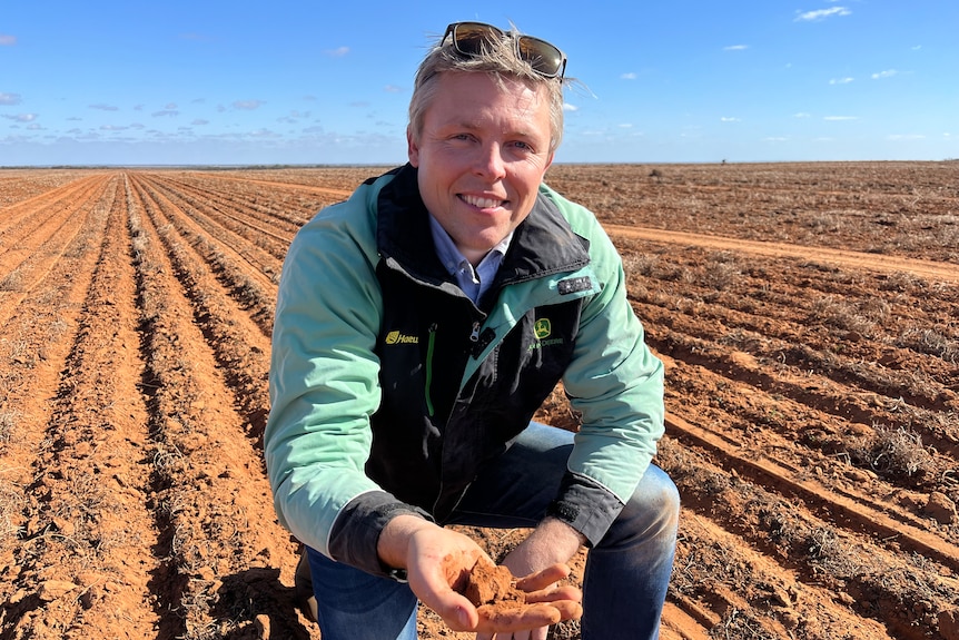 Daniel Linklater kneels in a paddock and is holding a handful of soil