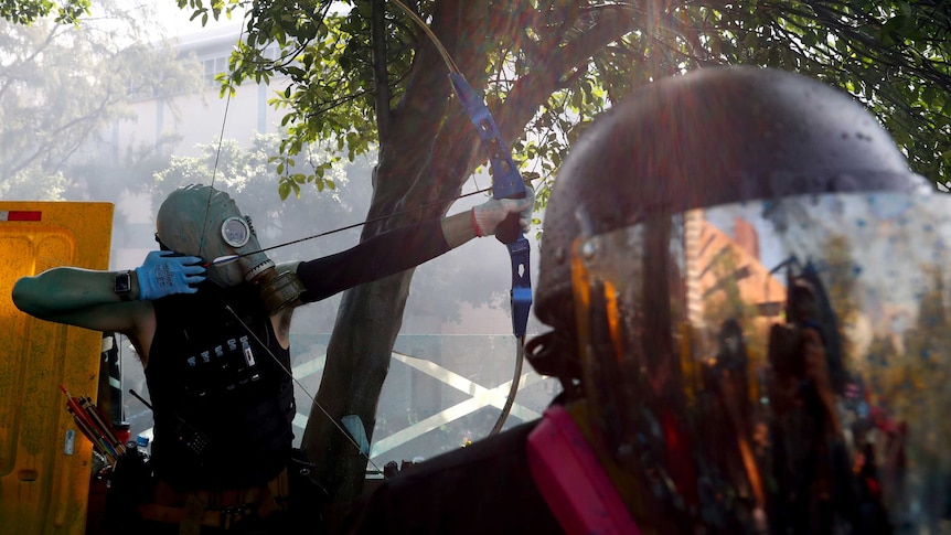 A protester dressed in a black singlet and an oxygen mask fires an arrow in Hong Kong.