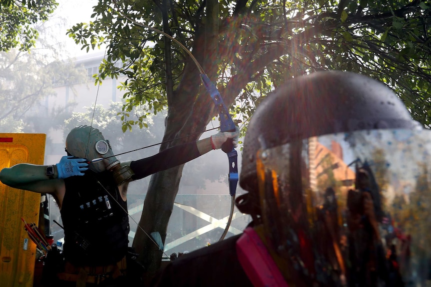 A protester dressed in a black singlet and an oxygen mask fires an arrow in Hong Kong.