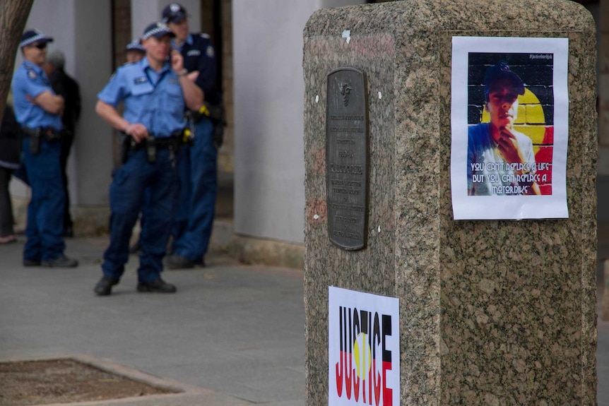 A poster of Elijah Doughty outside the Kalgoorlie courthouse, with a group of police officers in the background.