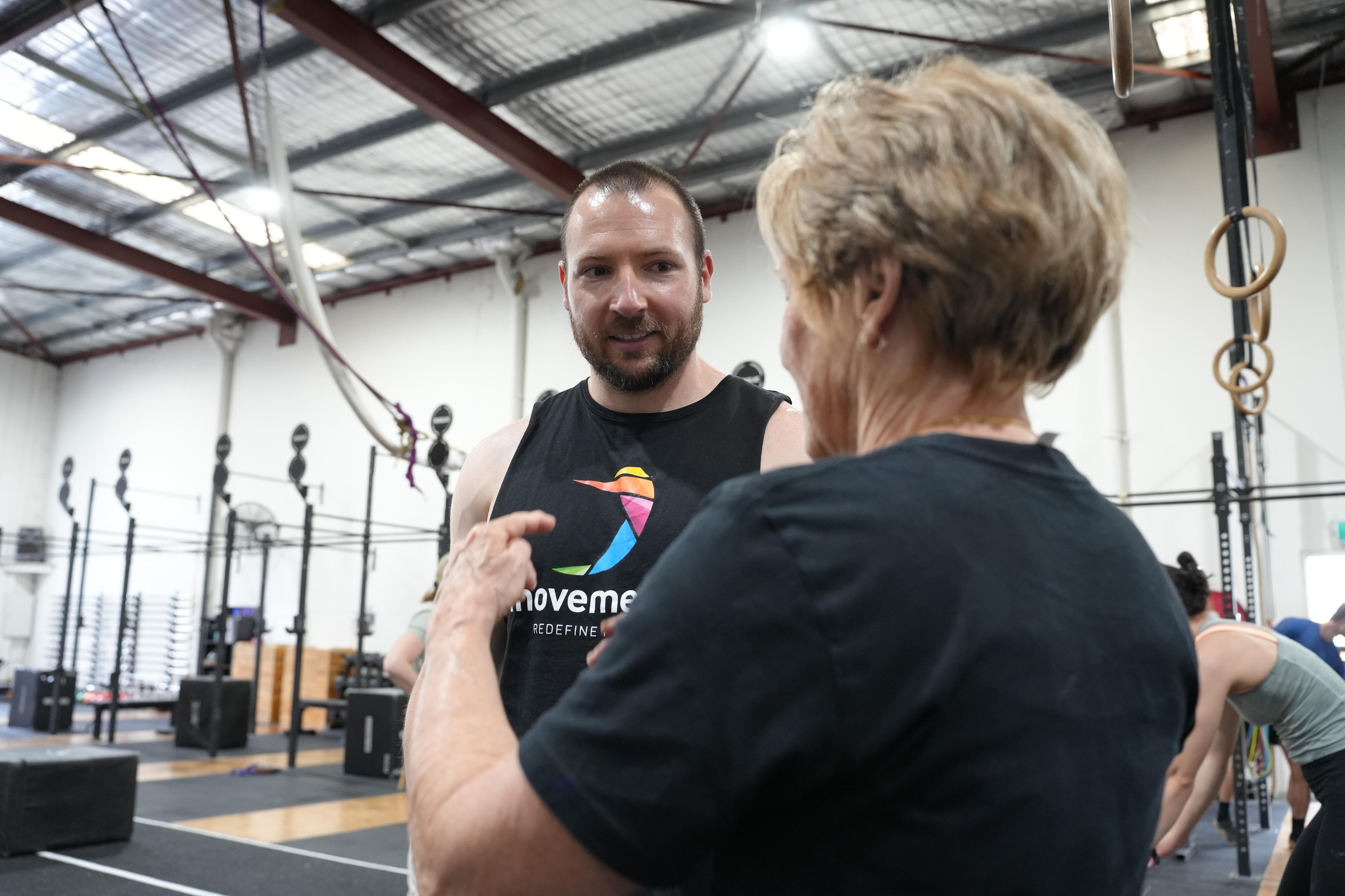 The back of a woman talking to a man wearing a black singlet top 