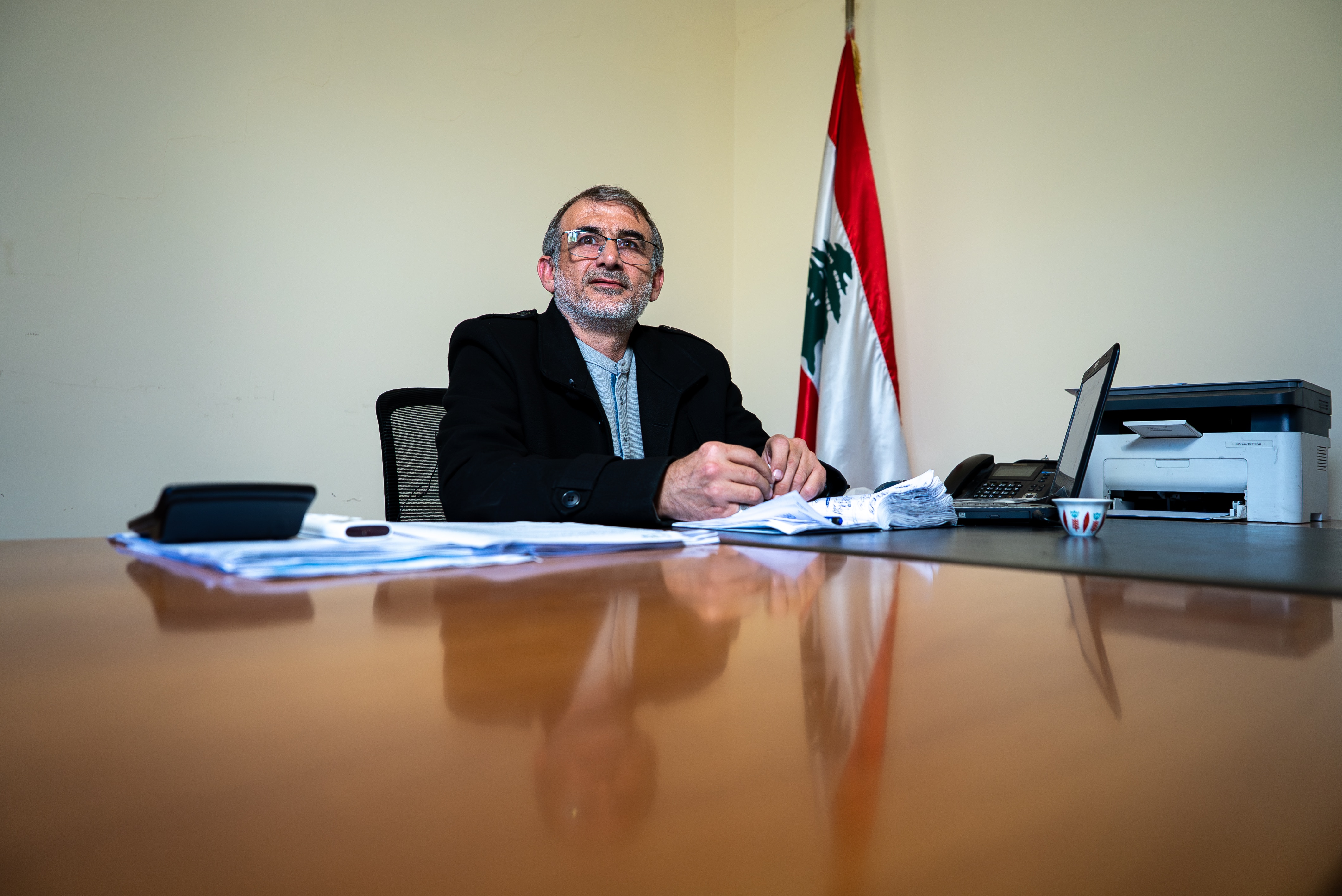 A man sitting at a desk with the flag of Lebanon behind him.