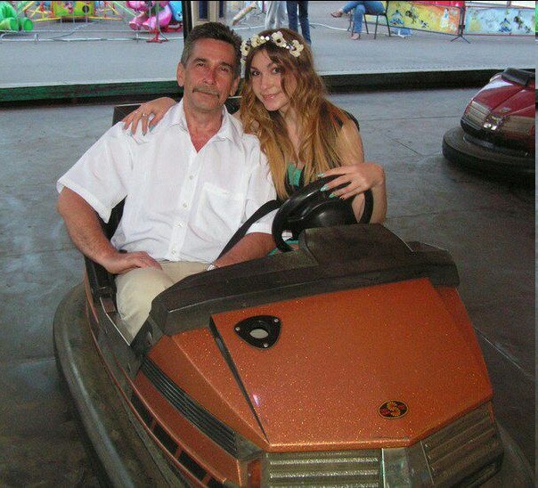 Pai e filha se abraçam enquanto estão sentados em um carro Dodge.