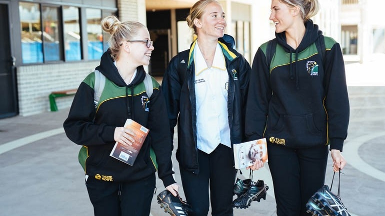 three young sportswomen in tracksuits walking carrying soccer boots