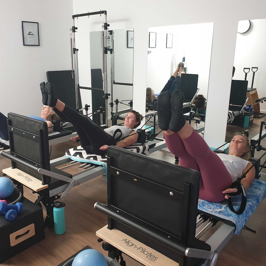 Women practice Pilates on exercise machines.