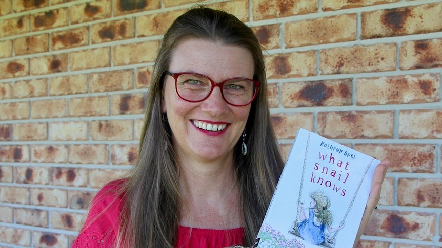 A woman wearing glasses holds a children's book.