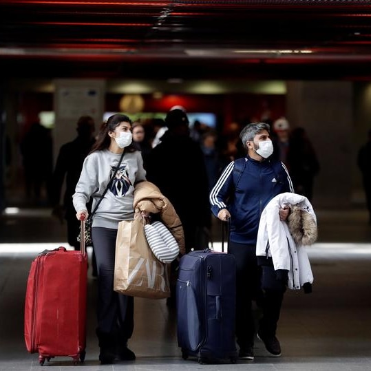 Passengers wearing face masks and rolling their suitcases through a railway station.
