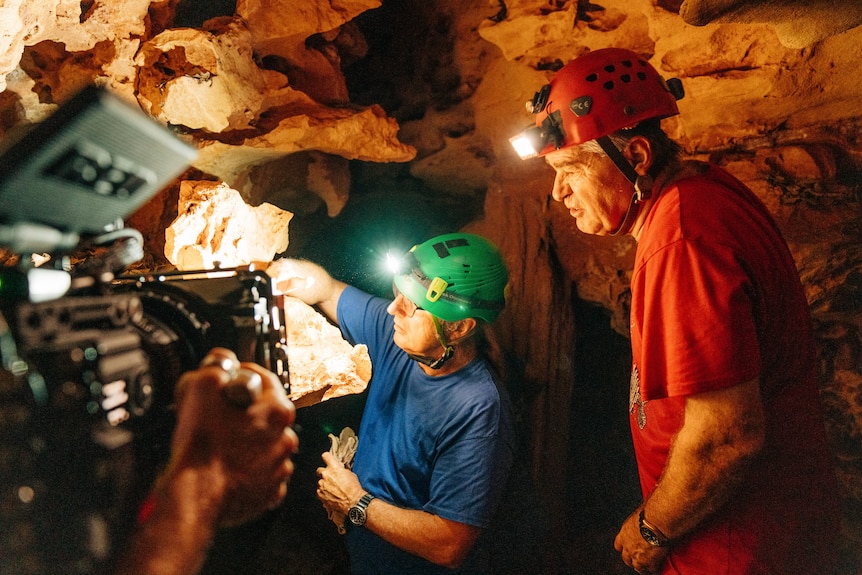 Two men wearing hard hats in a cave being filmed.
