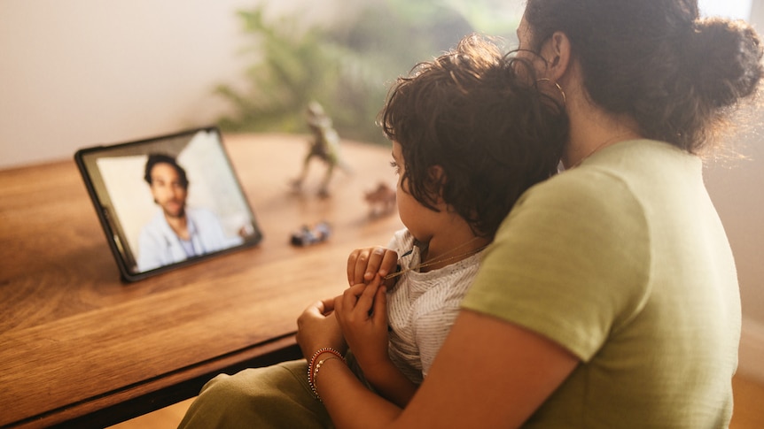 A generic stock photo of a mother and child on a telehealth appointment video call with a doctor.