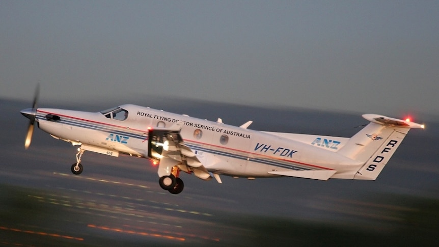 A light plane with the Royal Flying Doctor Service logo taking off the runway during the evening.