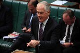 Malcolm Turnbull wears a white shirt with red and blue striped tie, Barnaby Joyce and Josh Frydenberg sit behind him.