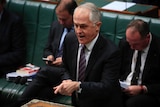 Malcolm Turnbull wears a white shirt with red and blue striped tie, Barnaby Joyce and Josh Frydenberg sit behind him.