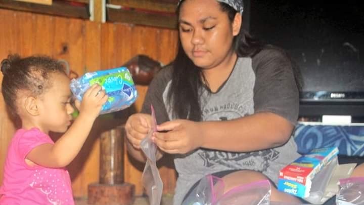 A Fijian woman in her teenage packing sanitary products with a toddler at home.