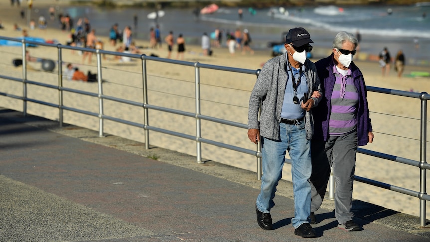 两个戴口罩的老人走在海滩边。