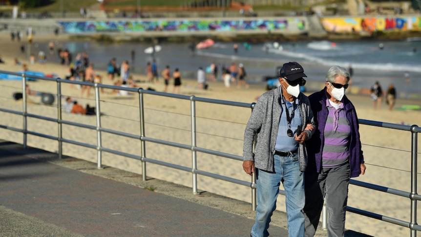 An elderly couple wearing masks walk on the Bondi beach boardwalk.