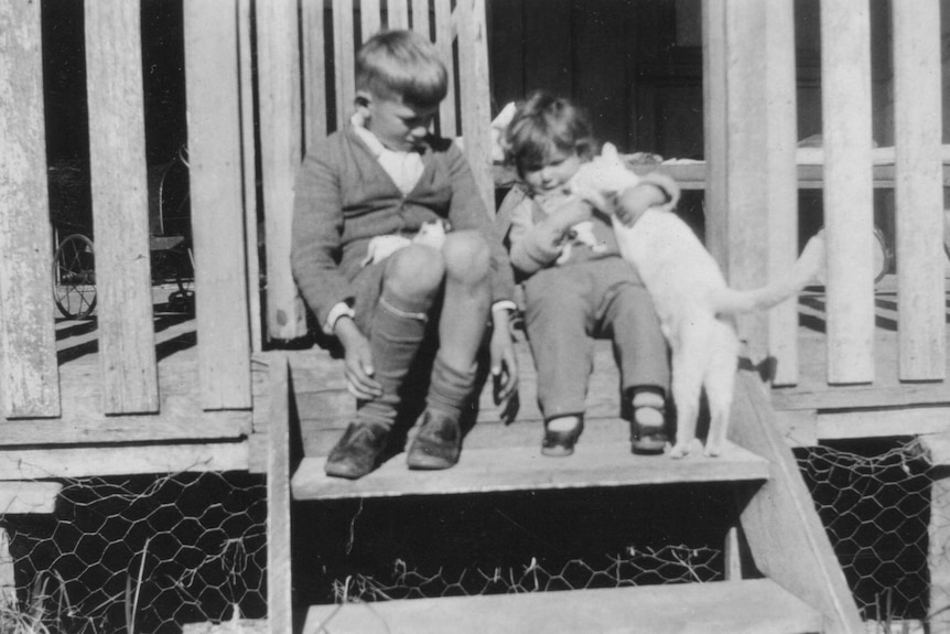 A black and white photograph of a young boy sitting next to a young girl on a set of verandah steps.