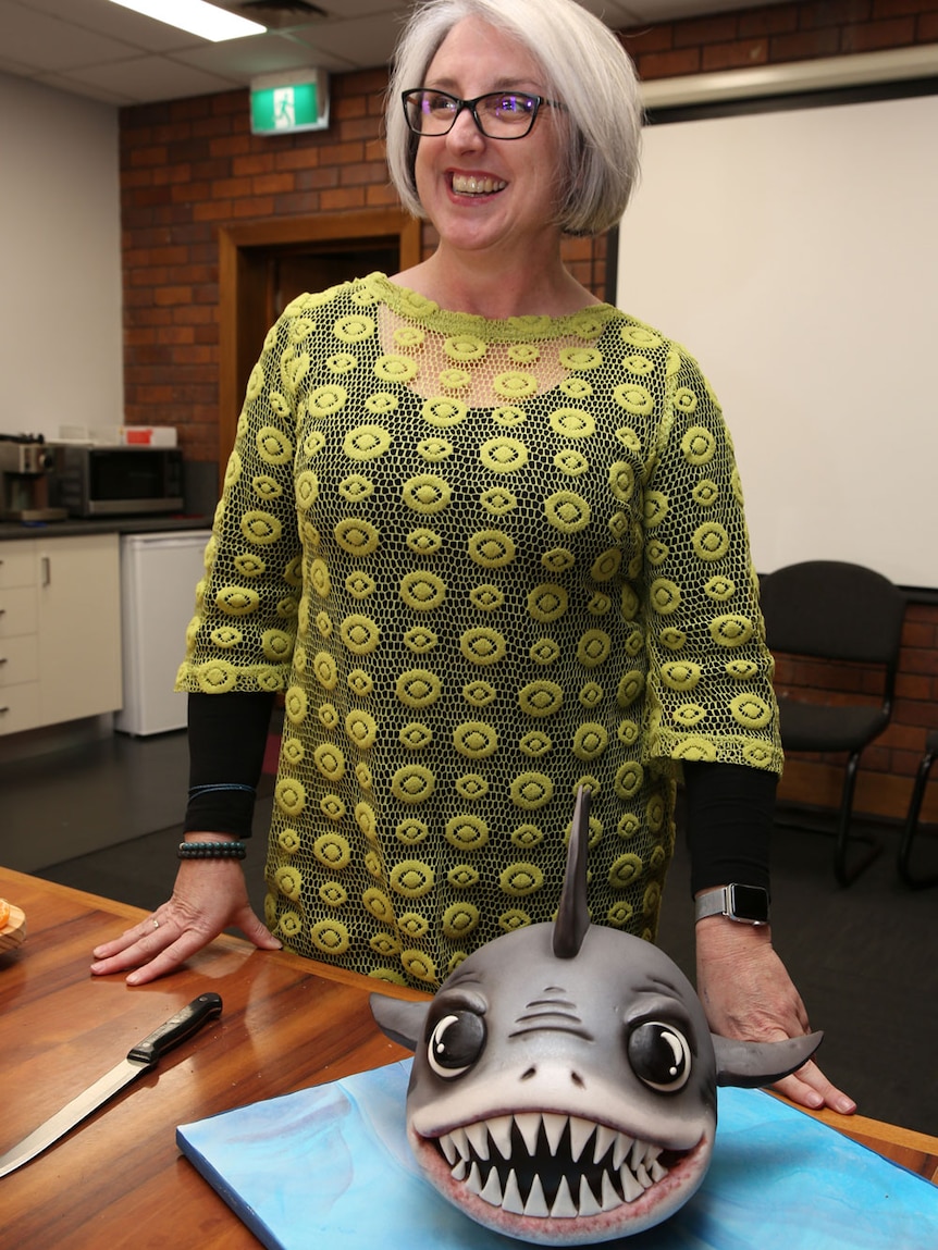 Justine Barwick stand smiling with a shark cake in front of her.