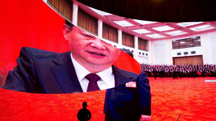 A child stands near a large screen showing photos of Chinese President Xi in China's Xinjiang region.