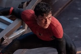 An unmasked Spider-Man is crouched in a low lunge, one hand on the ground between his legs and the other in the air behind him