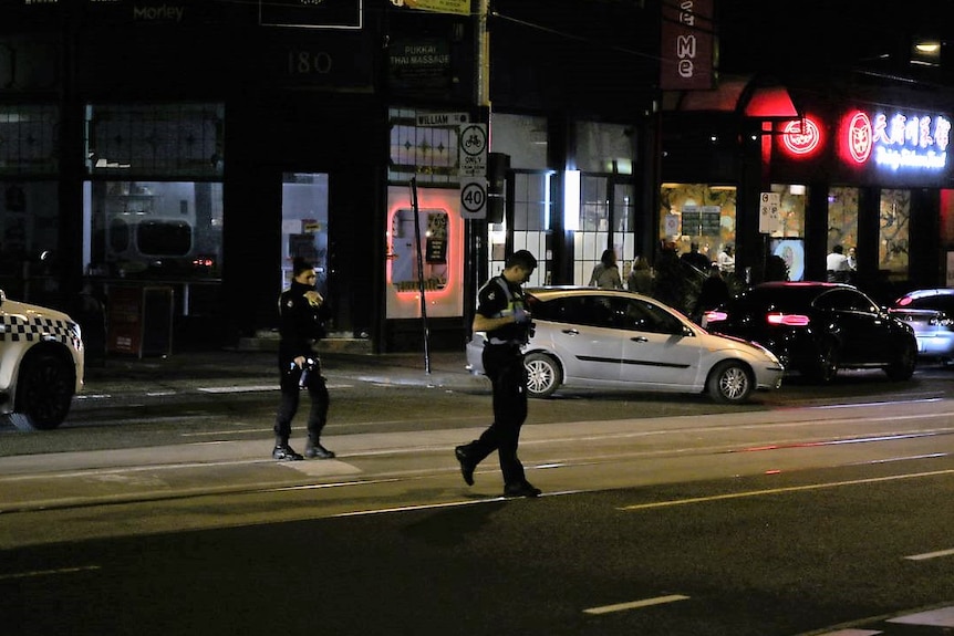 A male and a female police officer walk across a city road at night.