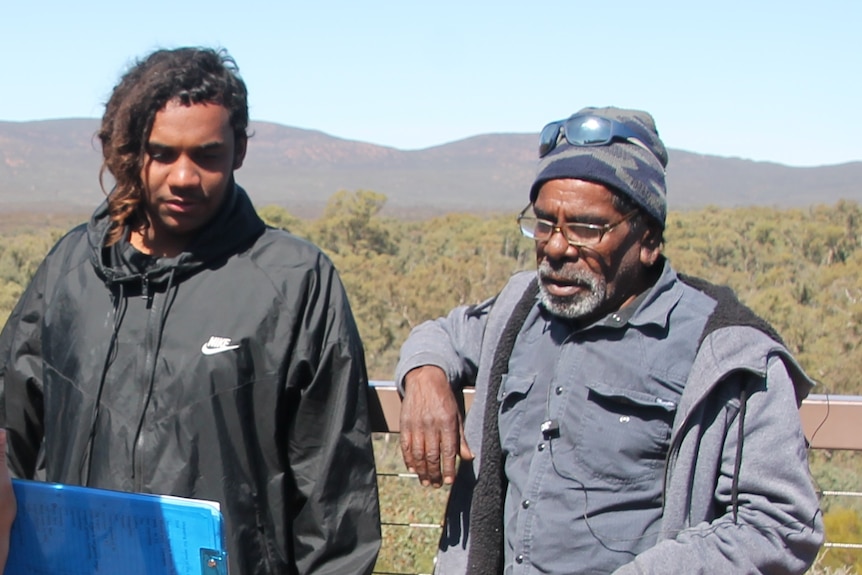 Two Indigenous men leaning against a fence talking.