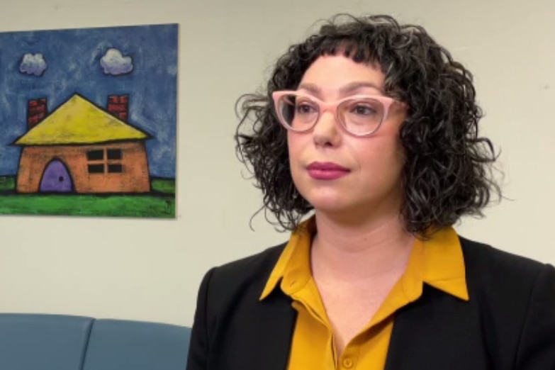 A woman with curly black hair and pink glasses looks off camera