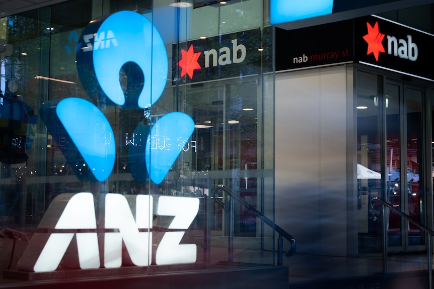People walk past bright light-up signs at the front of ANZ and NAB bank branches.