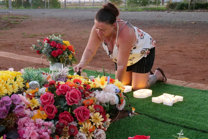 A woman kneeling a lighting a candle at a grave with flowers covering it