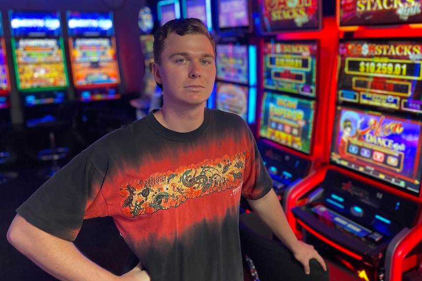 A young man is pictured in front of slotmachines, he looks serious. 