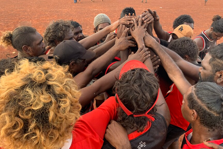Indigenous men put their hands in a huddle to build morale during a game