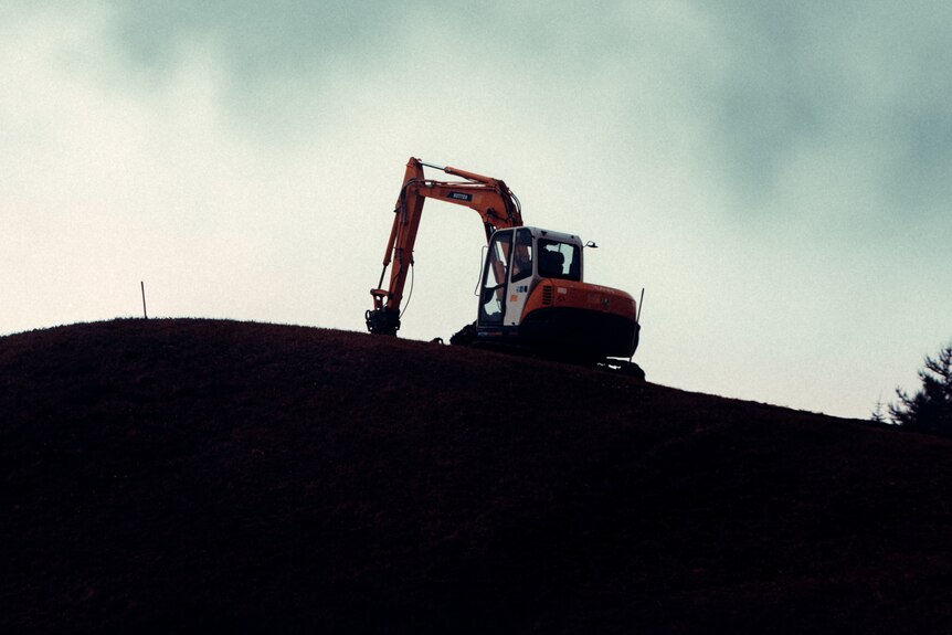 Excavator machine working in a barren field, unknown location.