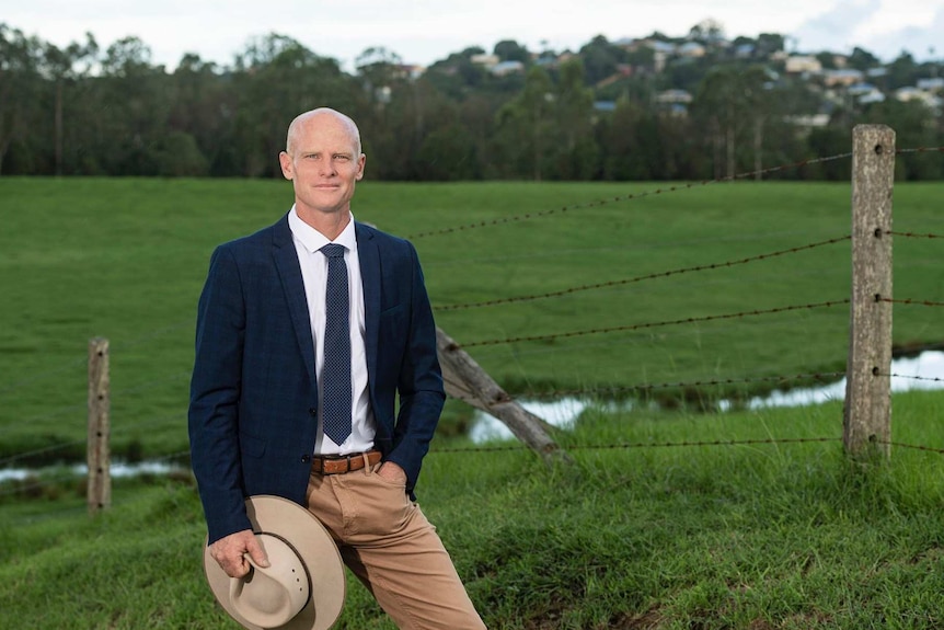 Man standing in field, in front of fence.