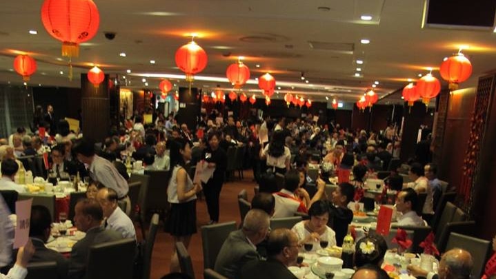 A large room filled with people eating, the ceiling decorated with red lanterns.