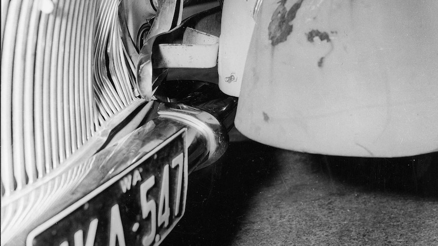 Black and white close-up of the front grill and headlight of John Button's damaged Simca car, next to another car.