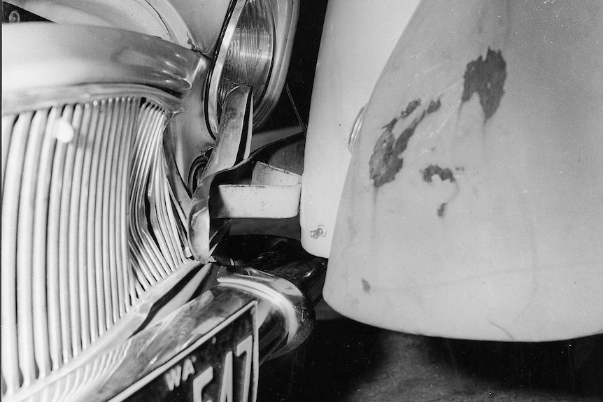 Black and white close-up of the front grill and headlight of John Button's damaged Simca car, next to another car.