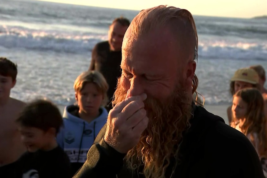 A man on the beach with his hand to his face