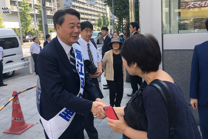 A candidate in Japan's upcoming elections shakes hands with people on the streets of Tokyo.