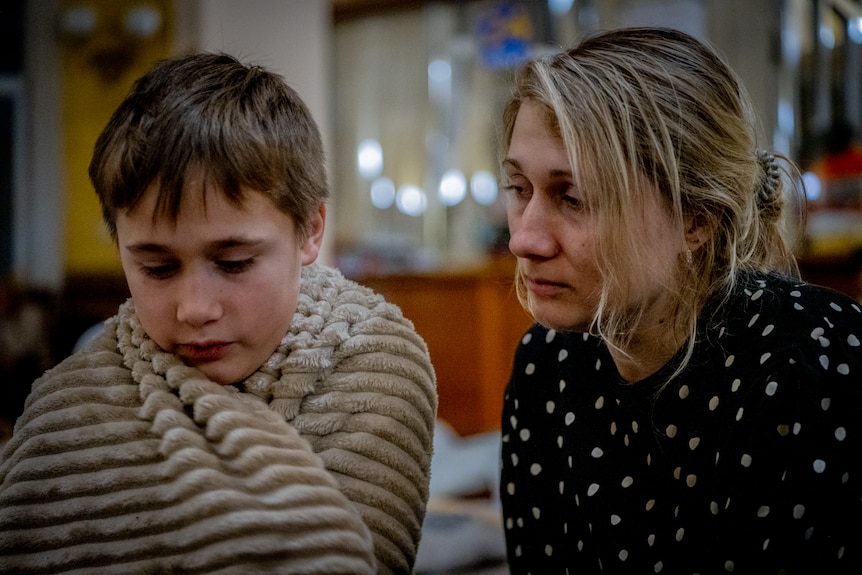 A young boy sits on the ground next to his mother